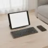 Clavier compact posé devant une tablette sur support, avec un téléphone à côté, sur une table en bois clair