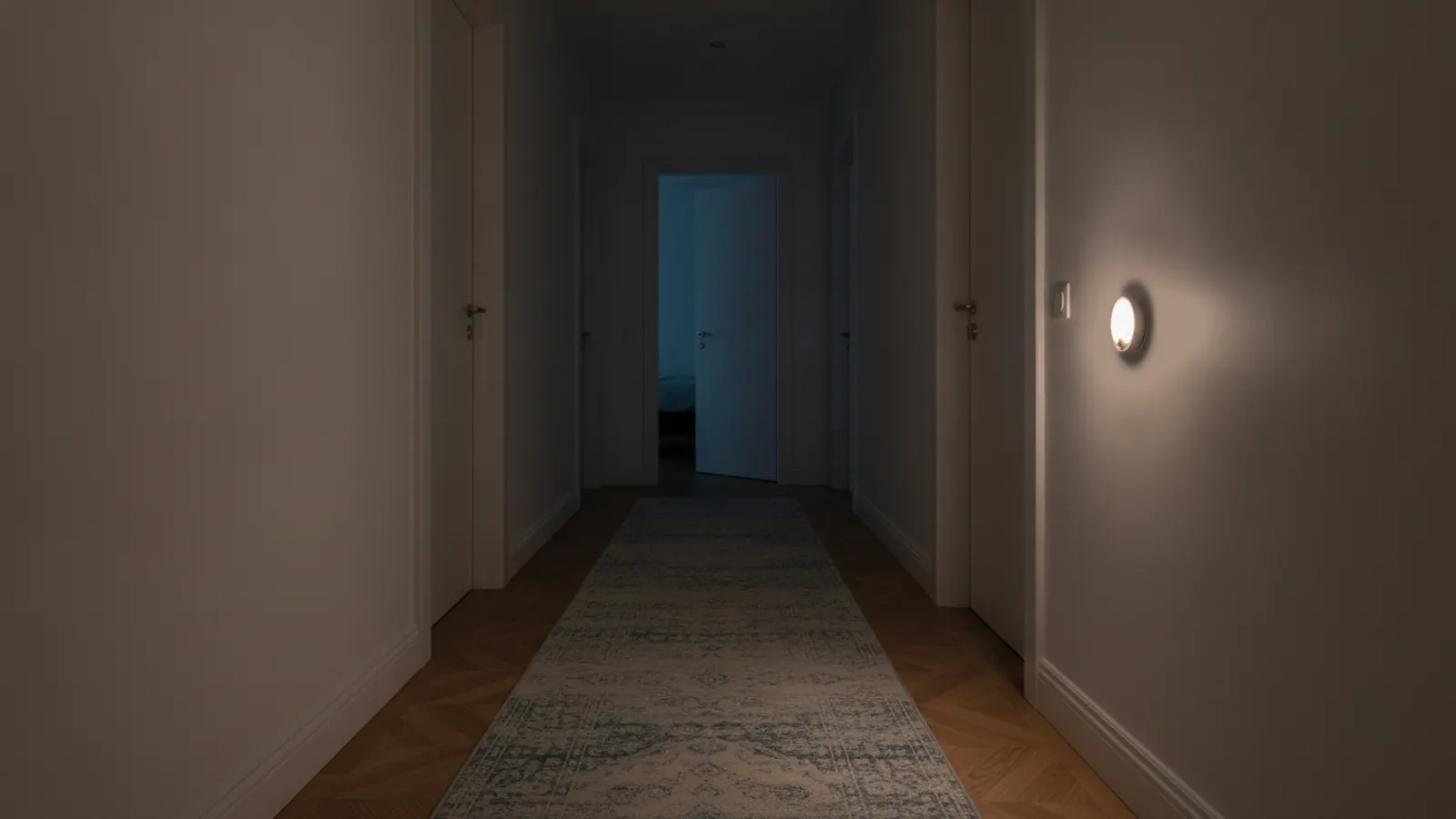 Couloir de maison la nuit, veilleuse allumée sur le mur de droite près d’une porte