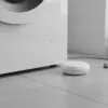 Détecteur posé sur le carrelage à côté d'un lave-linge blanc, près du tuyau d'arrivée d'eau