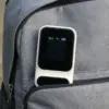 Boîtier crème et noir qui dépasse de la poche avant ouverte d’un sac à dos en tissu gris