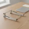 Support d'ordinateur en aluminium replié à plat, posé sur un bureau en bois clair