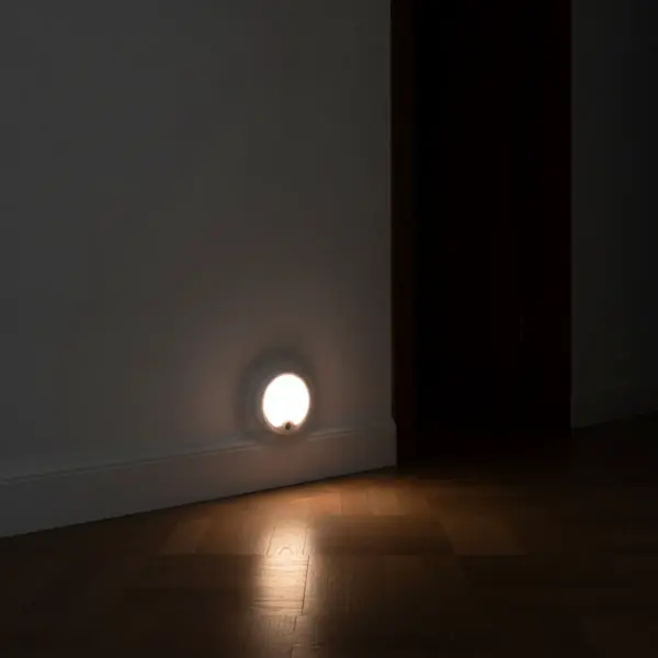 Veilleuse allumée au bas du mur d’un couloir, au-dessus de la plinthe, éclairant le parquet