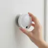 Main posant la veilleuse sur son disque métallique collé au mur, où elle tient par aimant