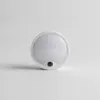Veilleuse LED ronde et blanche avec petit capteur noir, vue de face sur fond gris clair