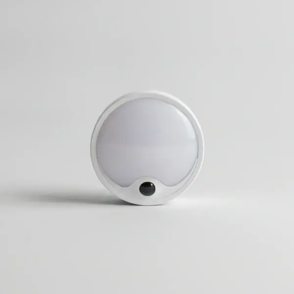 Veilleuse LED ronde et blanche avec petit capteur noir, vue de face sur fond gris clair