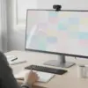 Webcam fixée sur le haut d'un écran pendant un appel vidéo, clavier et carnet sur la table de travail
